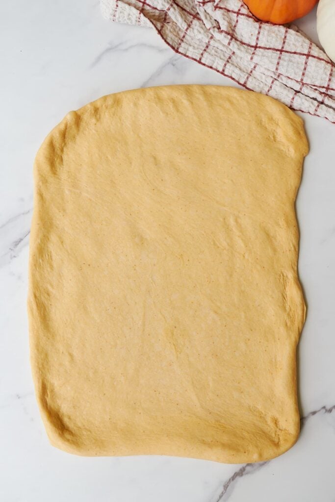 Sourdough Pumpkin Cinnamon Rolls rolled out into a rectangle next to a brown and white towel.