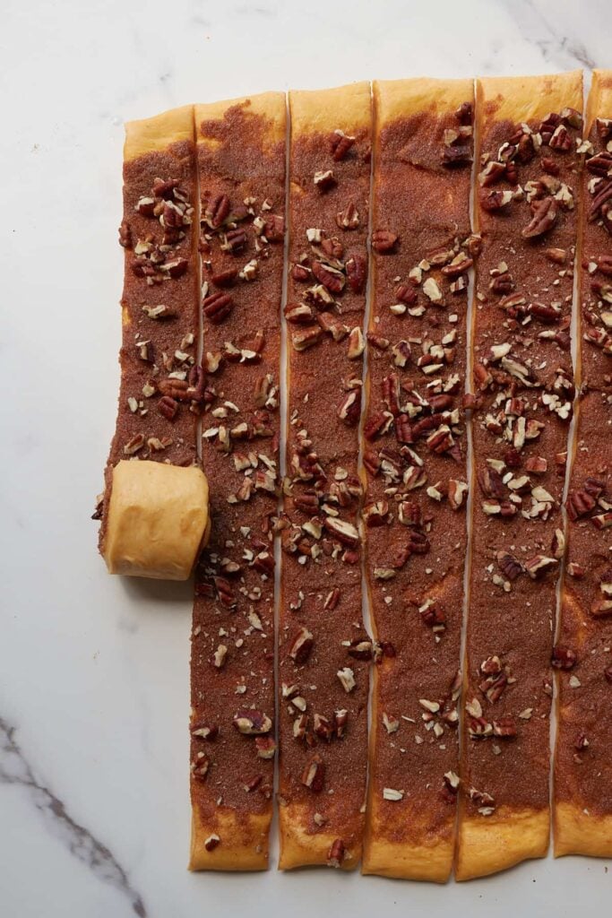 Rolling up strips of sourdough pumpkin cinnamon rolls.