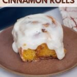 A brown plate with a sourdough pumpkin cinnamon roll with cream cheese frosting.