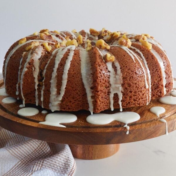 Sourdough coffee cake with a icing drizzle and walnuts sprinkled on top on a wooden cutting board.
