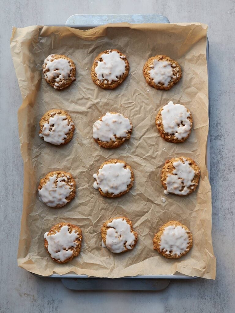 12 Sourdough Oatmeal Cookies with vanilla bean icing on a parchment lined sheet pan.