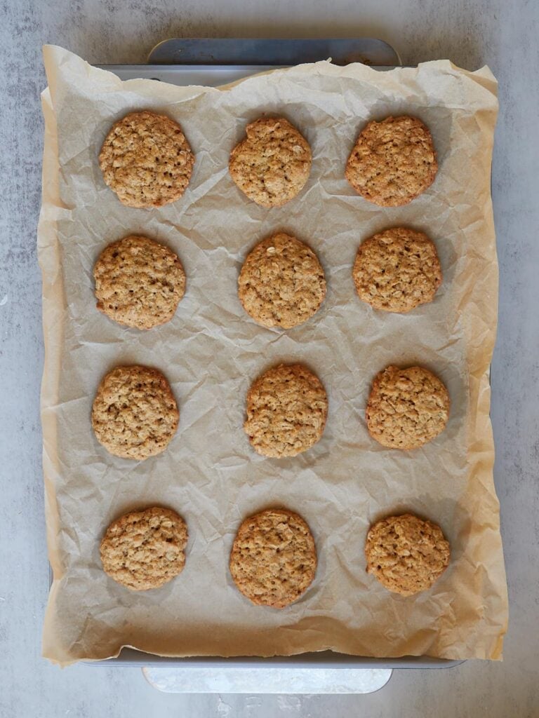 12 freshly baked Sourdough Oatmeal Cookies on a parchment lined sheet pan.