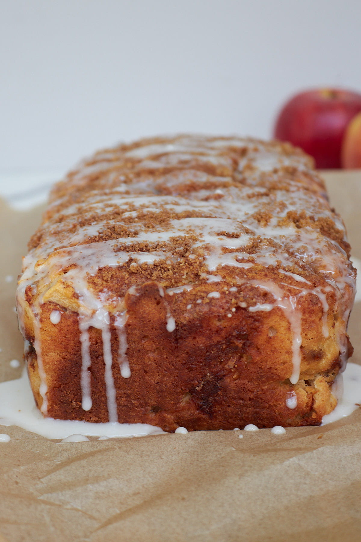 A loaf of Sourdough Apple Fritter Bread with vanilla icing on top on a piece of brown parchment paper.