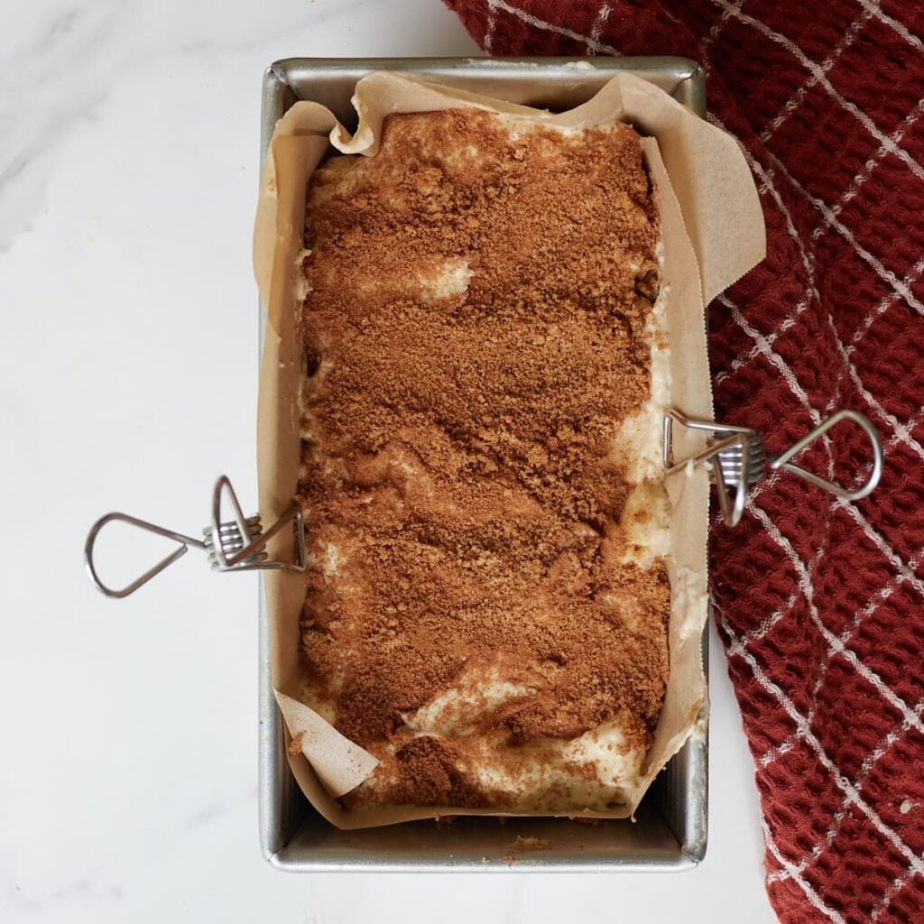 The final layer of sourdough apple fritter bread batter is added with the last layer of cinnamon sugar mixture.