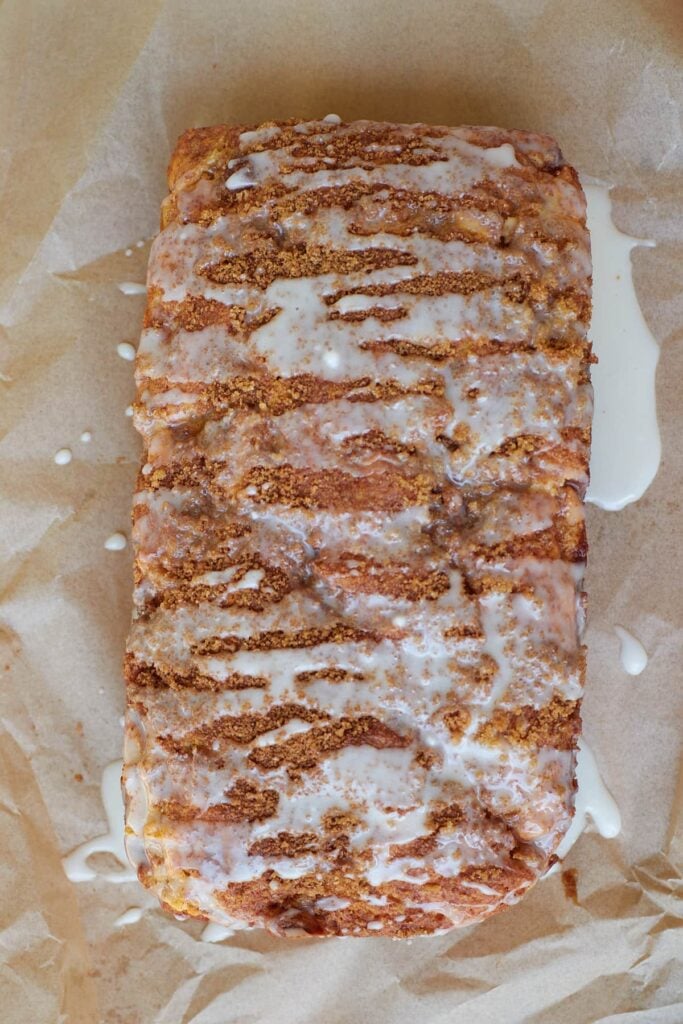 Vanilla icing drizzled on top of the freshly baked sourdough apple fritter bread on a piece of parchment paper.