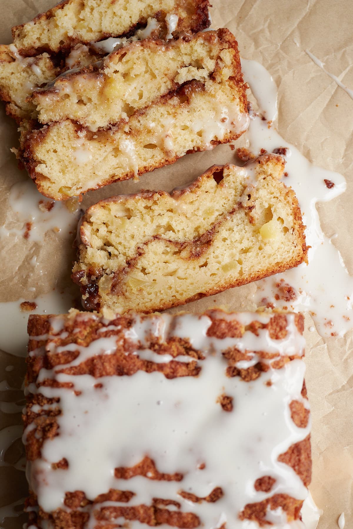 Slices of Sourdough Apple Fritter Bread with a vanilla glaze on a piece of brown parchment paper.