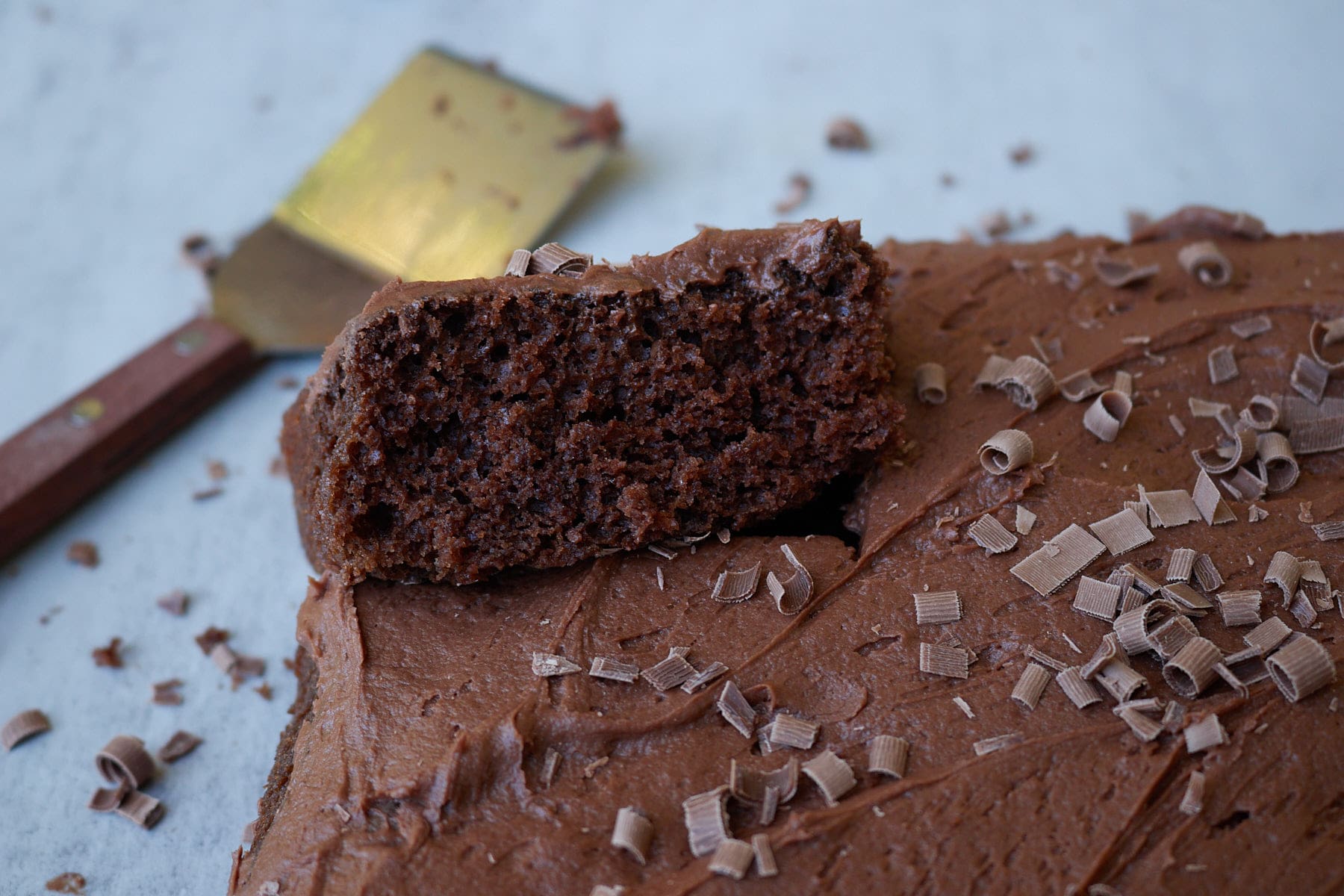 One slice taken out of Sourdough Chocolate Cake with Chocolate Buttercream frosting and chocolate shavings on top next to a cake cutter.