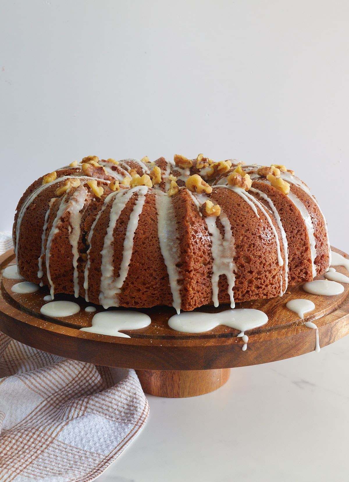 Sourdough coffee cake with a icing drizzle and walnuts sprinkled on top on a wooden cutting board.