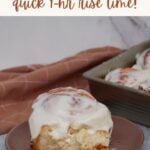 One sourdough discard cinnamon roll on a brown plate next to a 9x13 pan filled with sourdough discard cinnamon rolls.