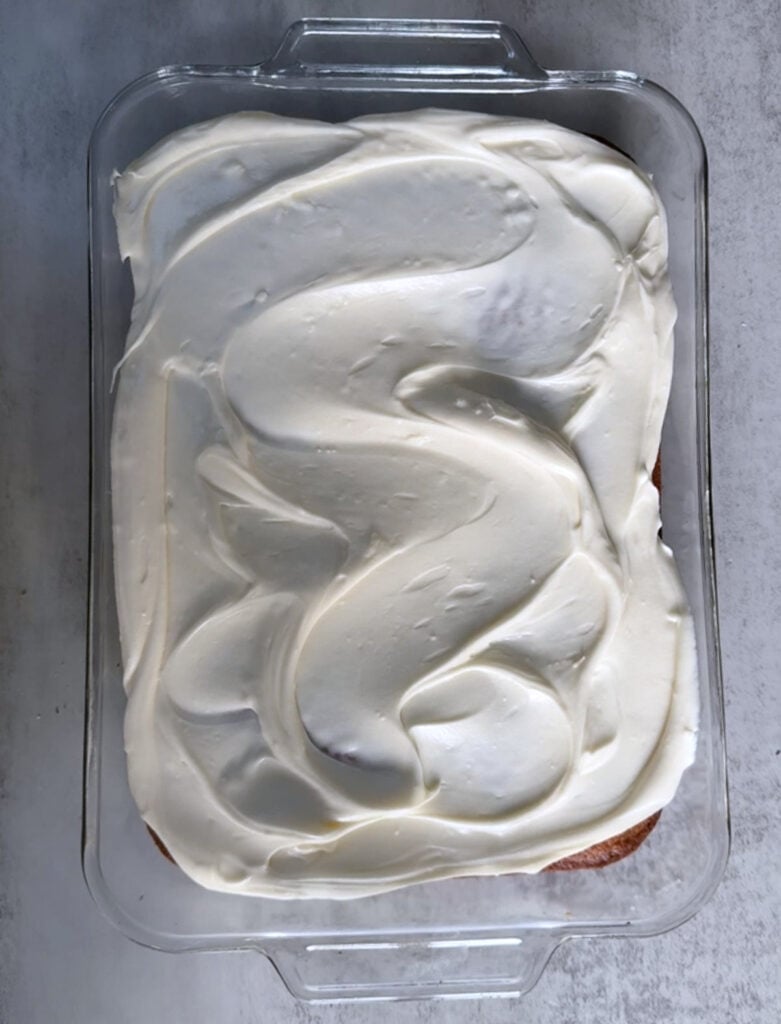 Frosting added to sourdough pumpkin cake in a clear 9x13 baking pan.