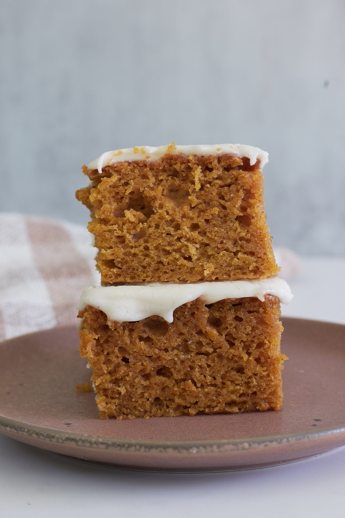 Two slices of Sourdough Pumpkin Cake stacked on top of each other on a brown plate.