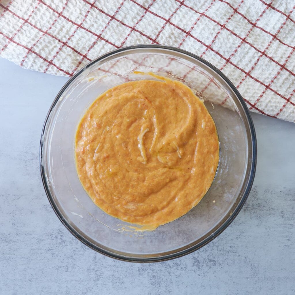 Wet ingredients for sourdough pumpkin cake in a clear bowl next to a white and red towel.