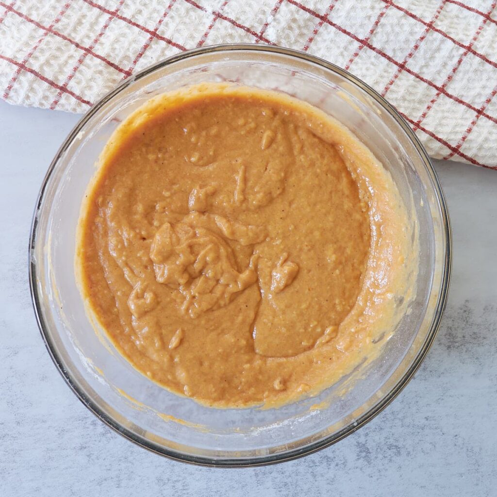 Batter for Sourdough Pumpkin cake in a clear bowl next to a white and red towel.