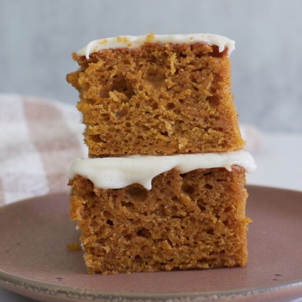 Two slices of Sourdough Pumpkin Cake stacked on top of each other on a brown plate.