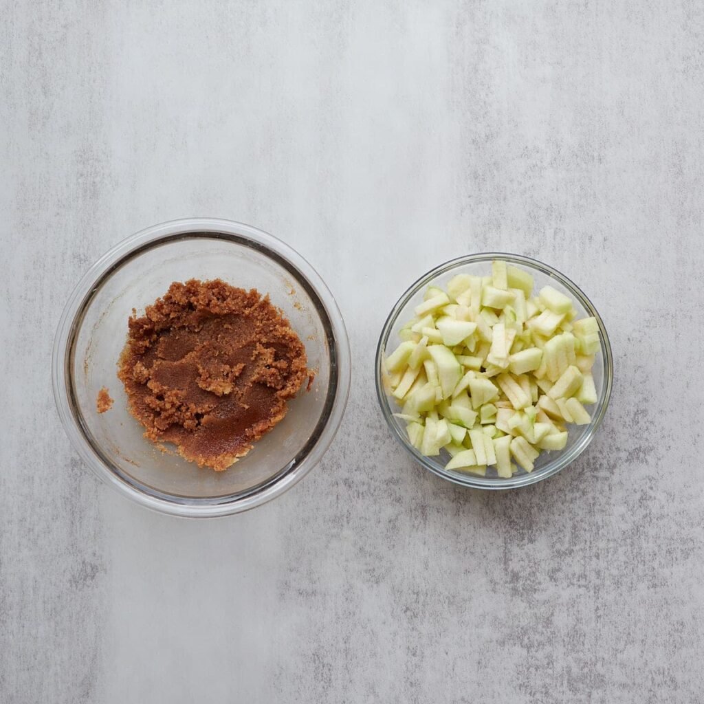 Filling for sourdough apple pie pull apart bread in a small clear bowl next to a bowl of diced apples.