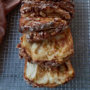 Sourdough Apple Pull-Apart Bread on a wire rack with a vanilla glaze with slices pulled out.