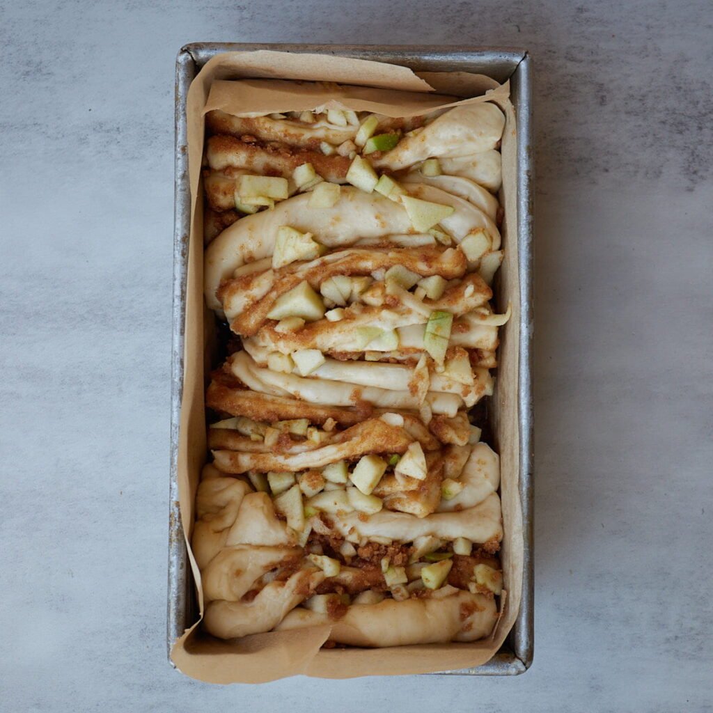 Layers of sourdough apple pie pull apart bread in the loaf pan.