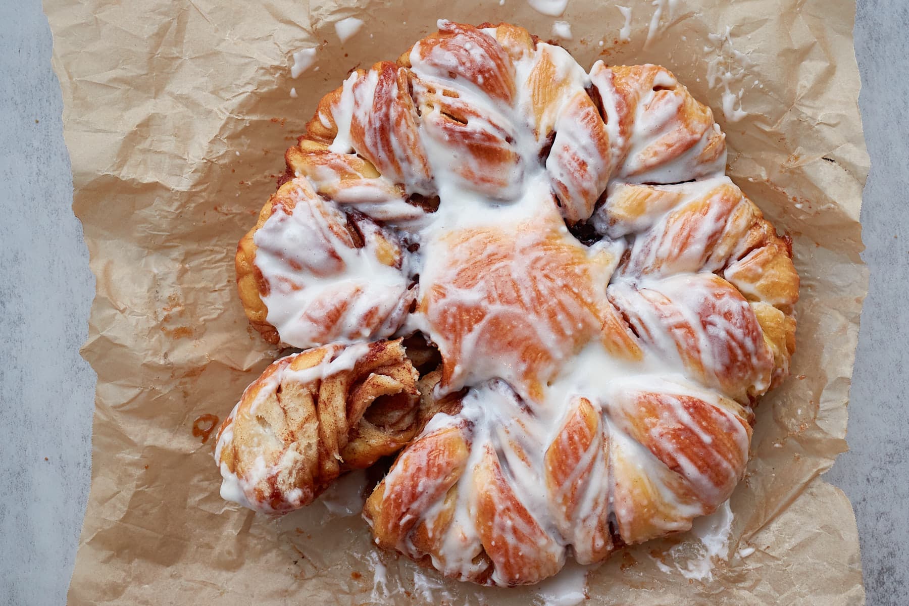 Sourdough Cinnamon Star Bread with cream cheese icing, with a section pulled off on brown parchment paper.