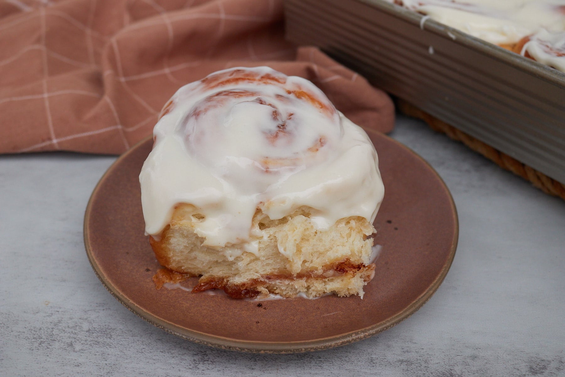 One sourdough discard cinnamon roll on a brown plate next to a 9x13 pan filled with sourdough discard cinnamon rolls.