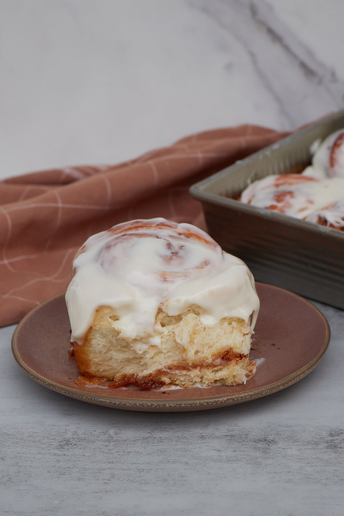 One sourdough discard cinnamon roll on a brown plate next to a 9x13 pan filled with sourdough discard cinnamon rolls.