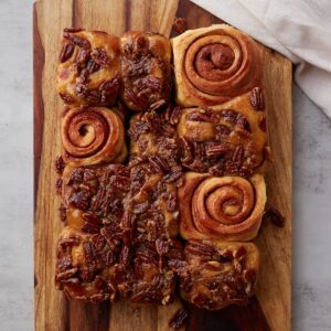 Sourdough sticky pecan buns on a wooden board with 3 sticky buns turned upside down to see the swirl.