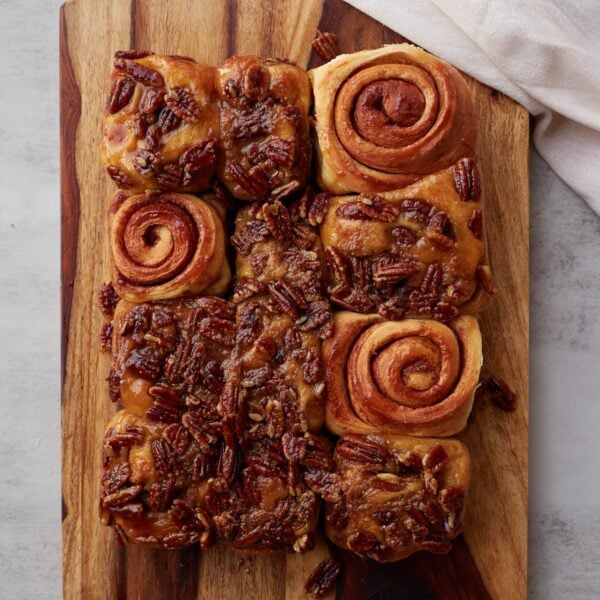 Sourdough sticky pecan buns on a wooden board with 3 sticky buns turned upside down to see the swirl.