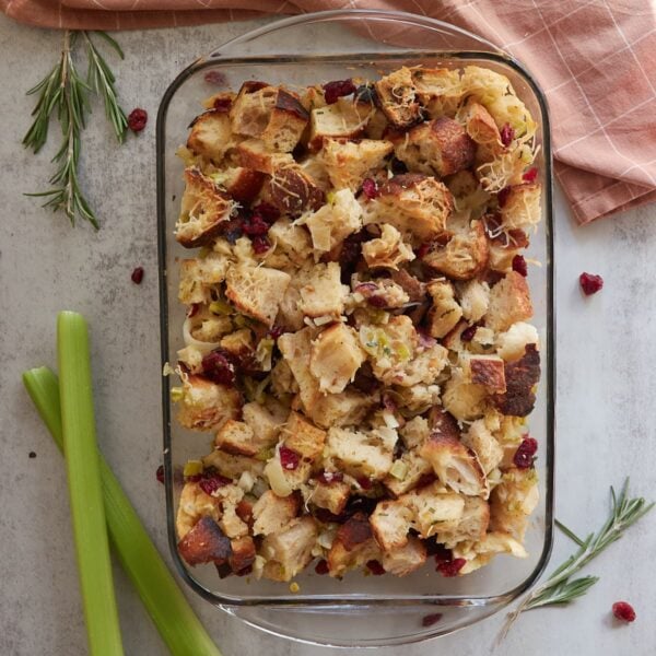 Sourdough stuffing in a glass 9x13 pan with a gold spoon inside and next to a brown cloth napkin.