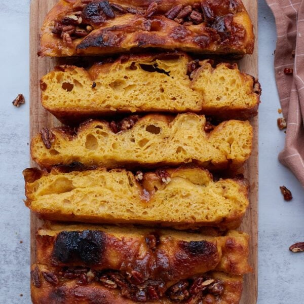3 slices of sourdough sweet potato focaccia on their sides on a wooden cutting board with pecans scattered around.