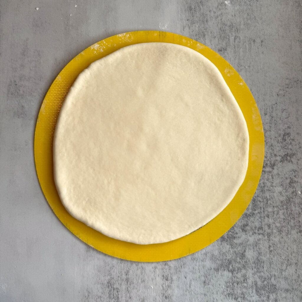 Cheesy Sourdough Star Bread dough rolled out into a round shape on top of a round silicone baking mat.