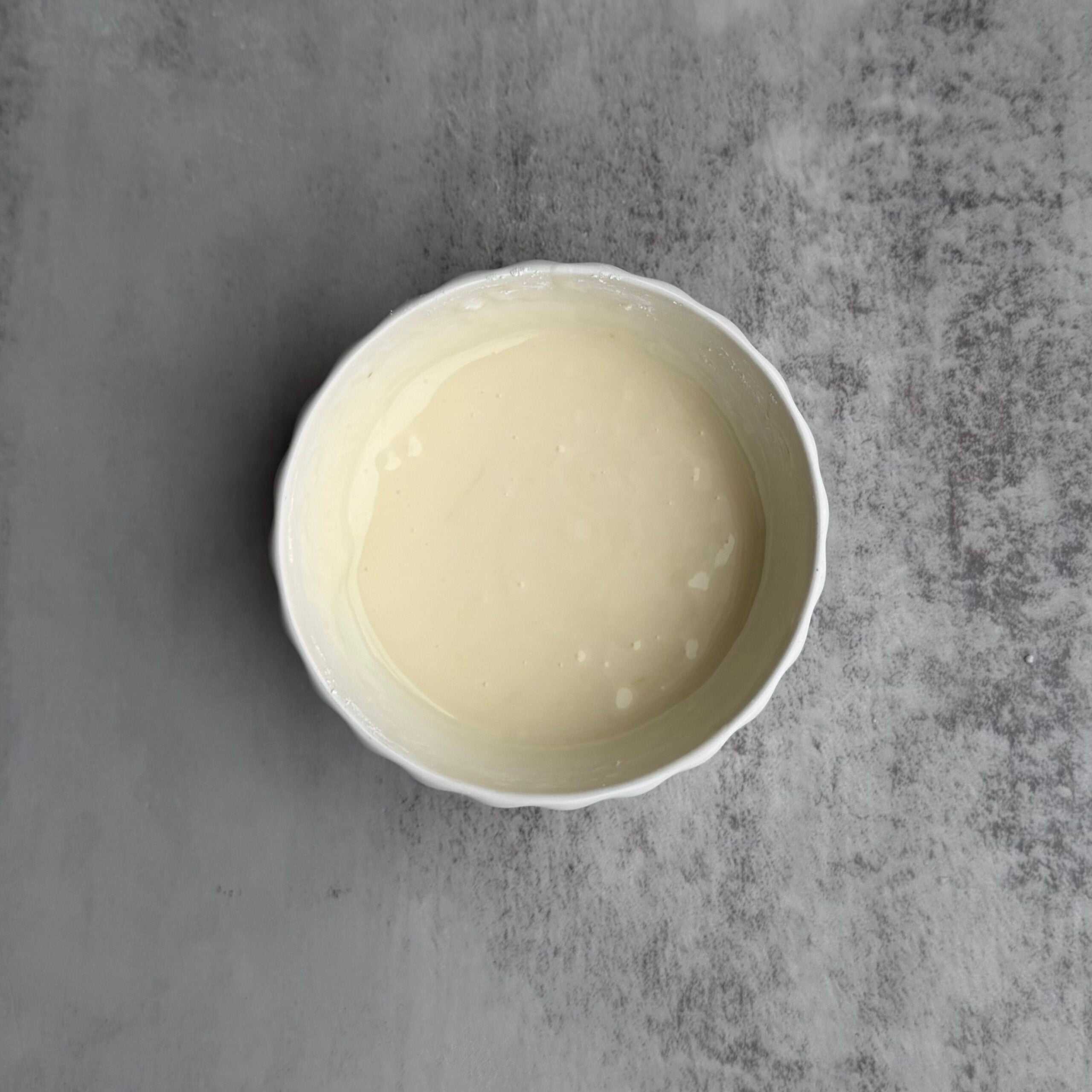 Orange glaze in a small white bowl on a gray counter.