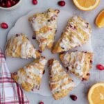 Six Sourdough cranberry orange scones on a white round platter with oranges and cranberries scattered around.