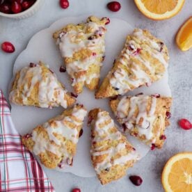 Six Sourdough cranberry orange scones on a white round platter with oranges and cranberries scattered around.