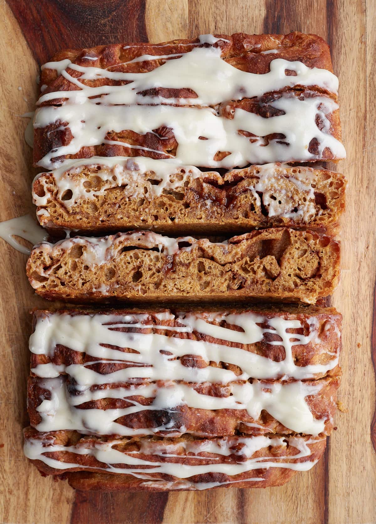 Sourdough gingerbread cinnamon roll focaccia with cream cheese icing on a wooden cutting board.