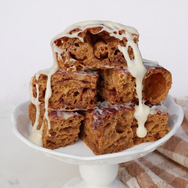 Slices of sourdough gingerbread focaccia with cream cheese icing on a white cake stand.