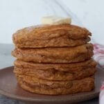 A stack of four sourdough gingerbread pancakes on a plate with a chunk of butter on top.