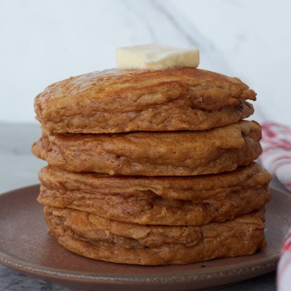 A stack of four sourdough gingerbread pancakes on a plate with a chunk of butter on top.