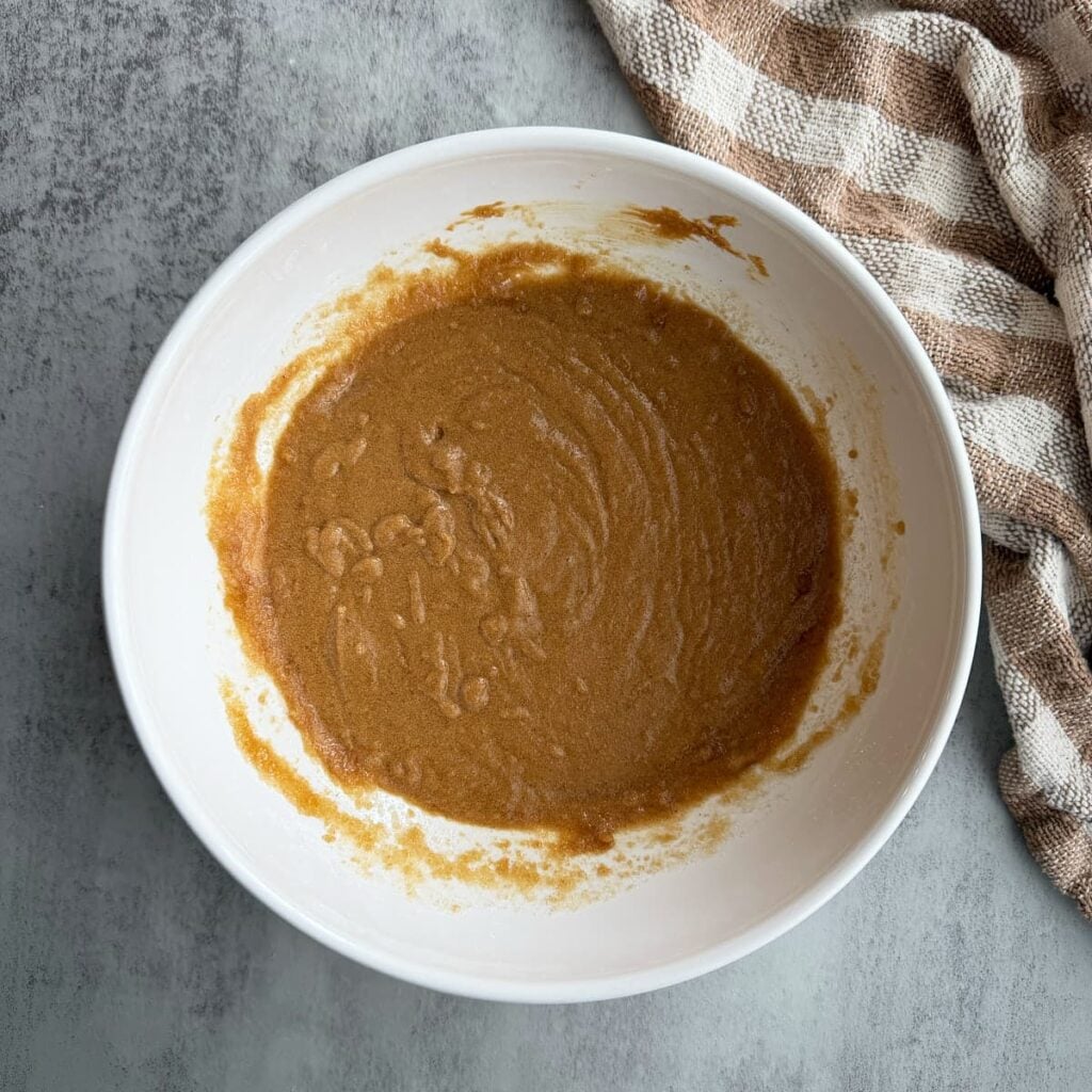 Sugar, brown butter and peanut butter mixed together in a white bowl for sourdough peanut butter cookies.