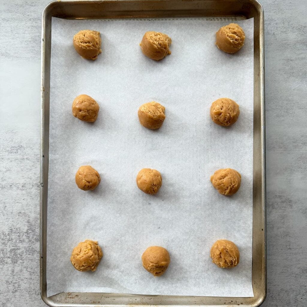 12 sourdough peanut butter cookie dough balls on a parchment lined baking sheet.