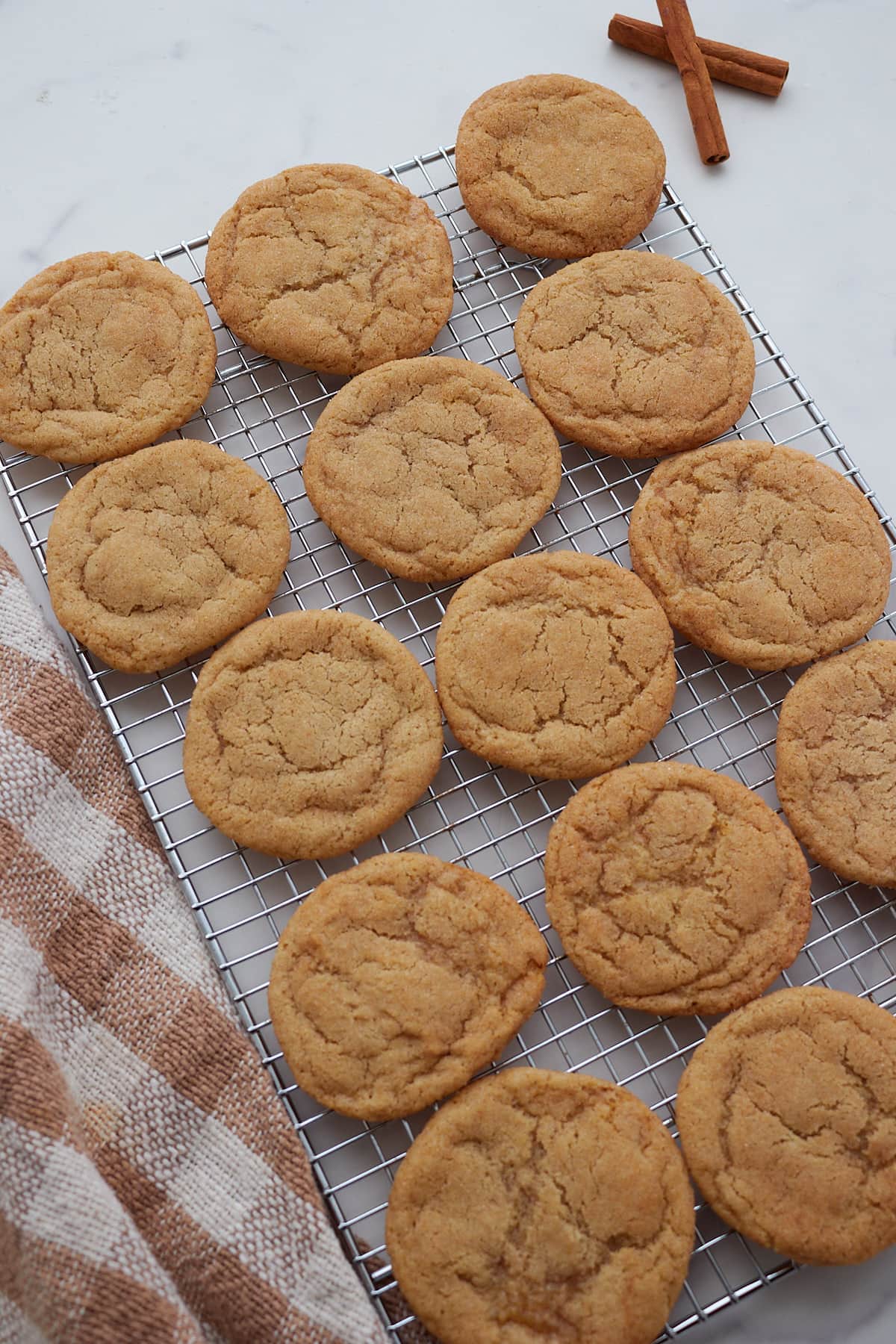 Sourdough Snickerdoodle cookies on a wire rack next to a white and brown towel.