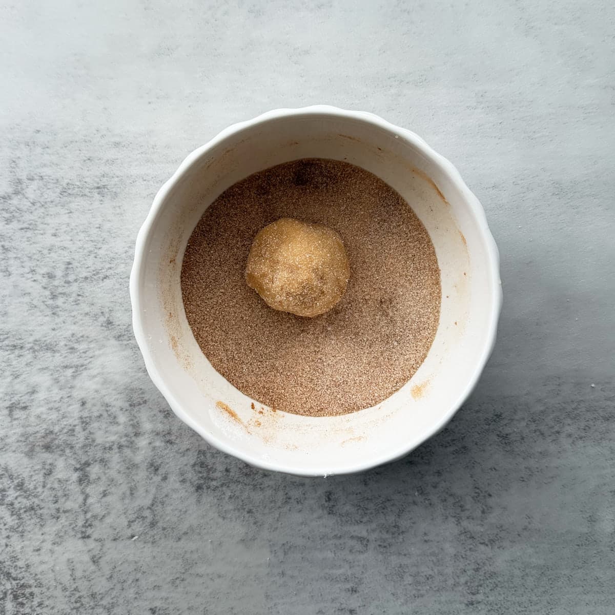 One sourdough snickerdoodle cookie dough ball in a bowl of cinnamon and sugar.