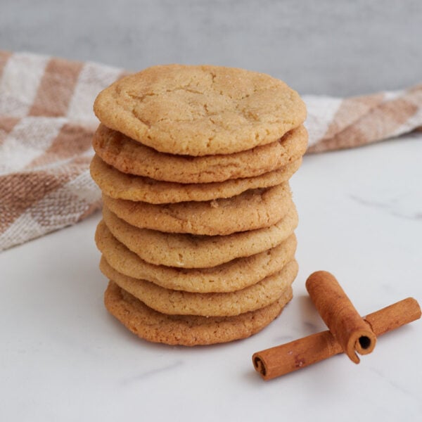 Sourdough Snickerdoodle Cookies stacked on top of each other next to cinnamon sticks.