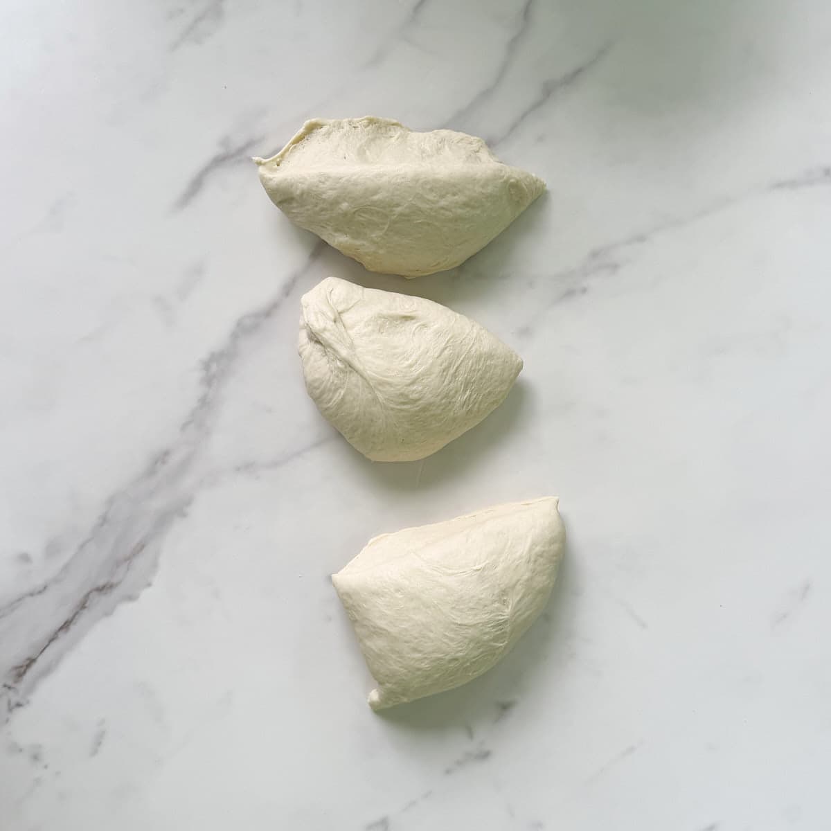 Sourdough discard pretzel bite dough after rising, divided into 3 equal parts on a marble surface.