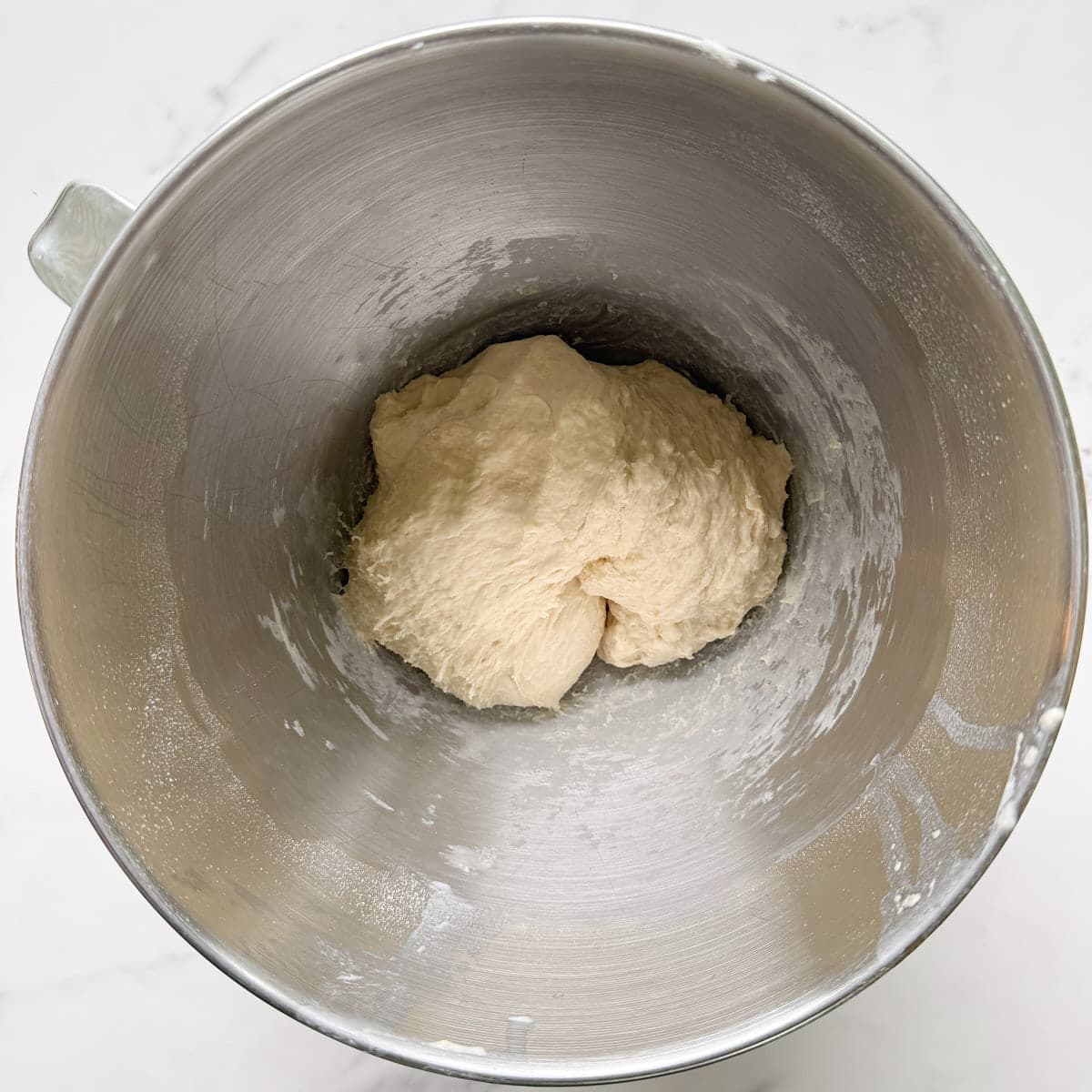 Sourdough discard pretzel bites dough in a metal kitchen aid bowl after kneading, on a white counter.