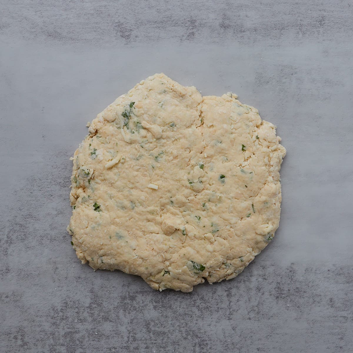 garlic scone dough shaped into an 8" circle on a counter.