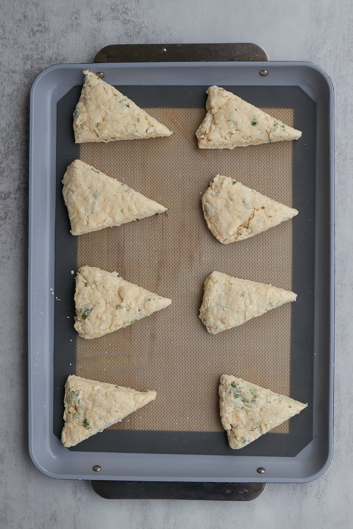 eight garlic scone wedges laid out on a baking sheet before baking.