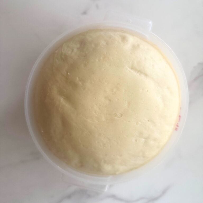 Top-down photo of sourdough monkey bread dough after a rise in a straight edge container with marble background. 