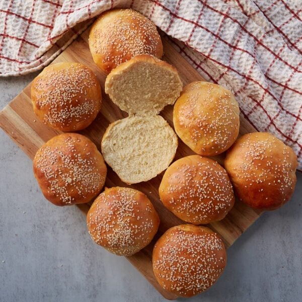 Discard hamburger buns arranged on a wooden tray, one bun is sliced open.
