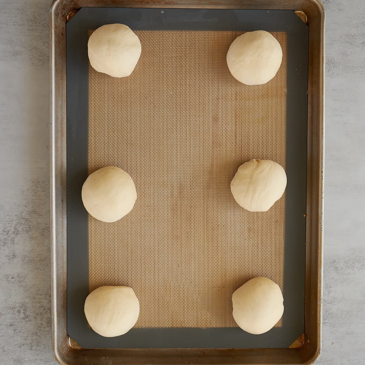 6 hamburger dough balls placed on a silicone lined mat. 