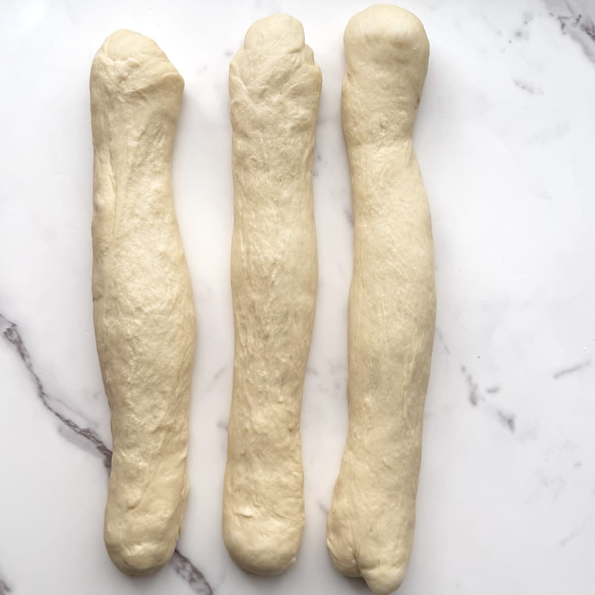Sourdough monkey bread dough divided into three equal parts and rolled into 15" logs on a marble counter.