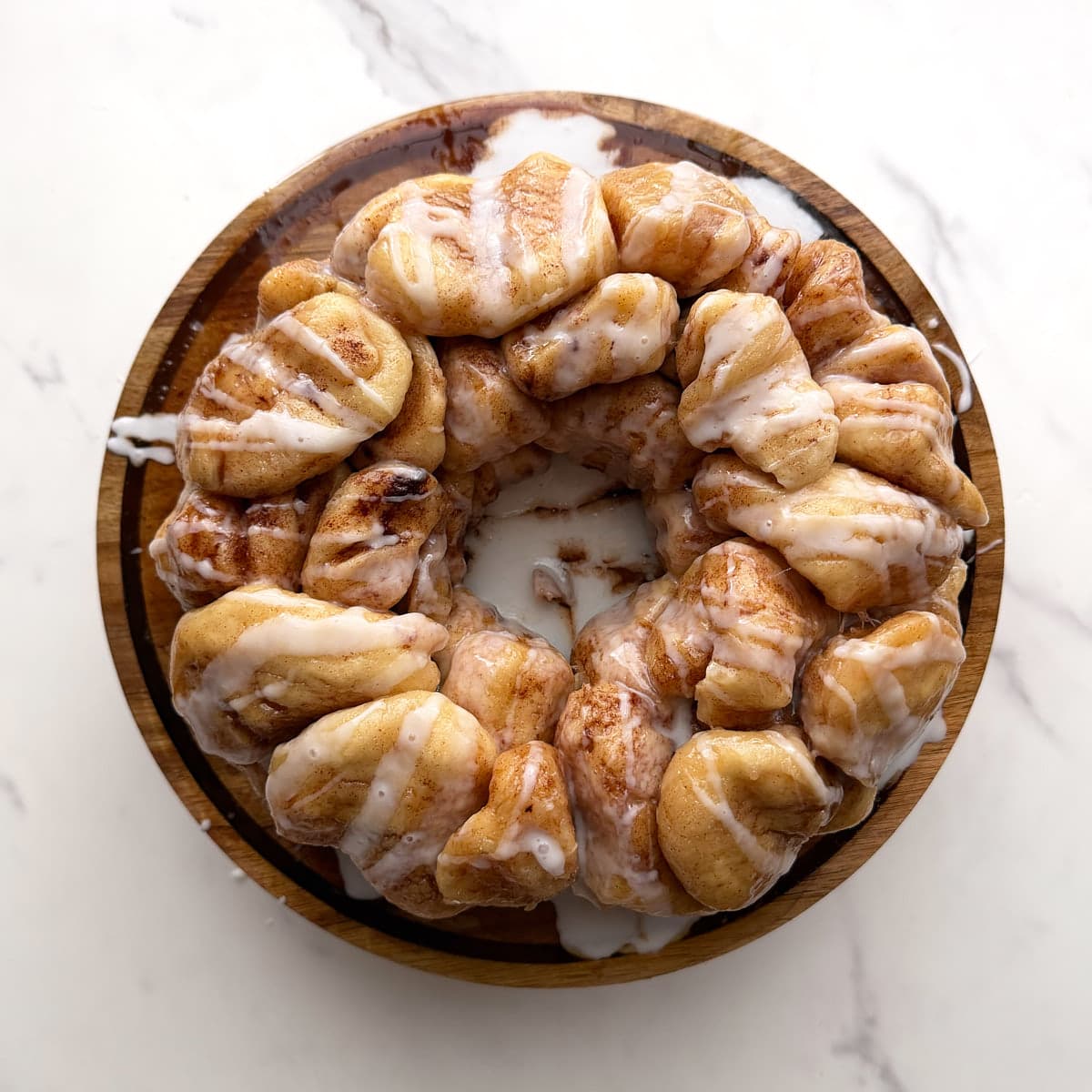 Sourdough monkey bread displayed on a wooden plate with icing drizzled on top.